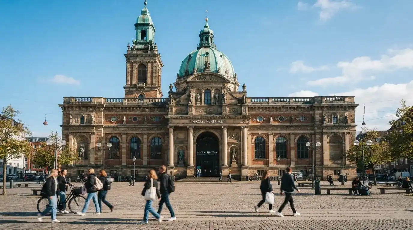 En historisk bygning i København med grøn kobbertag og kolonner i klart dagslys, set fra pladsen foran.